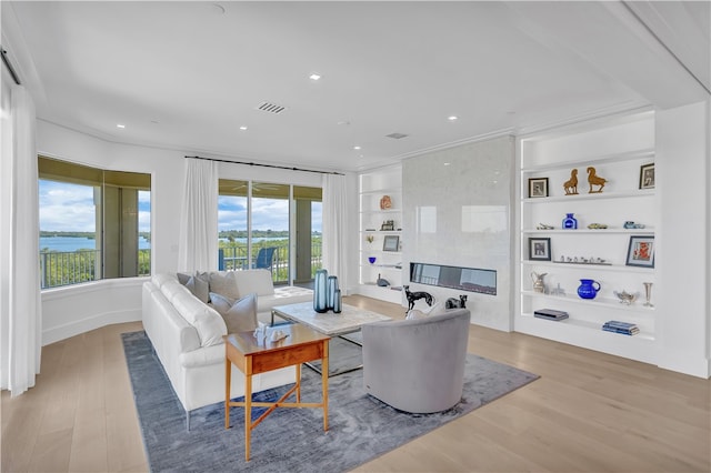 living room featuring built in features, light wood-type flooring, a water view, and plenty of natural light