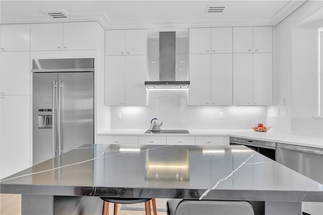 kitchen with tasteful backsplash, wall chimney range hood, appliances with stainless steel finishes, a kitchen breakfast bar, and white cabinets