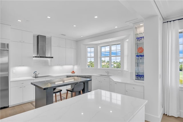 kitchen featuring stainless steel appliances, a kitchen island, white cabinetry, light hardwood / wood-style floors, and wall chimney exhaust hood