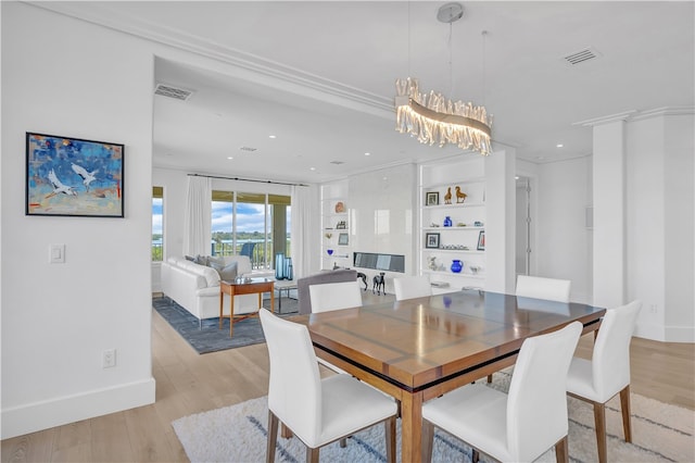 dining space featuring built in shelves, a chandelier, light wood-type flooring, and crown molding