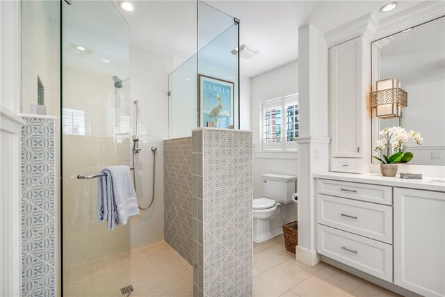 bathroom featuring toilet, vanity, tile patterned flooring, and a tile shower