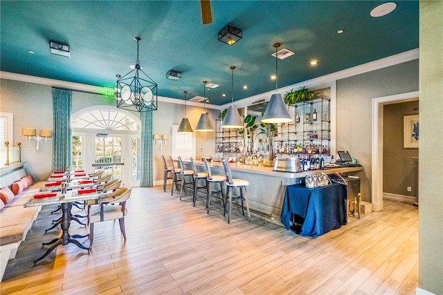 bar with pendant lighting, an inviting chandelier, crown molding, and light wood-type flooring