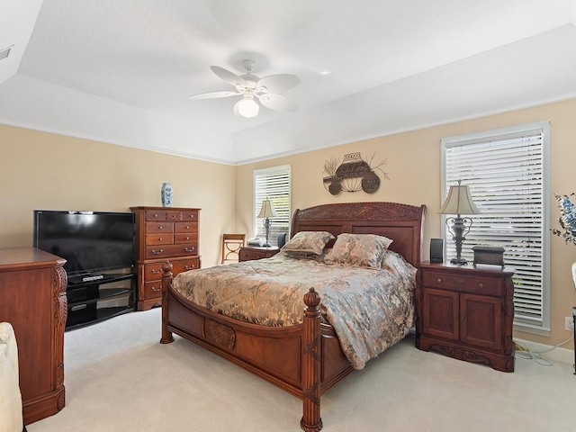 bedroom with light colored carpet, a raised ceiling, and ceiling fan