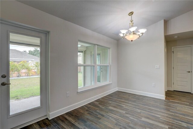 unfurnished dining area featuring baseboards, an inviting chandelier, and dark wood-style flooring