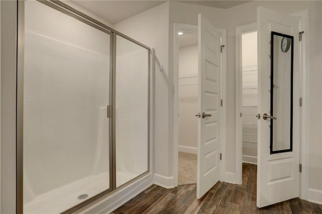 full bath featuring baseboards, wood finished floors, a shower stall, and a walk in closet