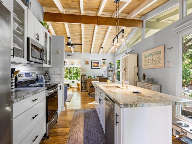 kitchen featuring lofted ceiling with beams, sink, an island with sink, appliances with stainless steel finishes, and white cabinetry