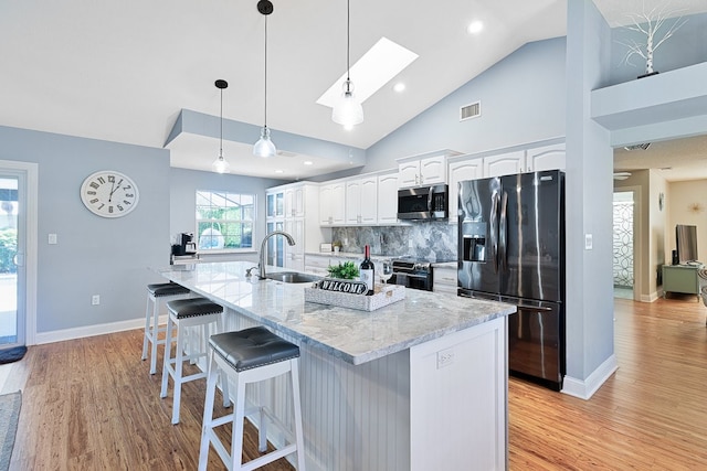 kitchen with appliances with stainless steel finishes, white cabinetry, sink, a large island with sink, and light stone counters