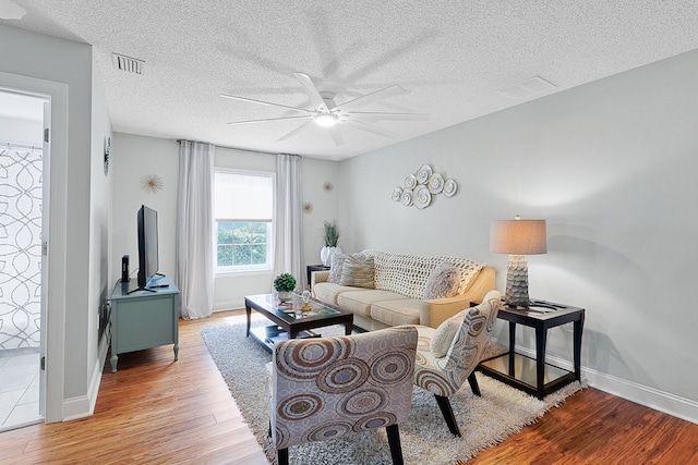 living room with light hardwood / wood-style floors, a textured ceiling, and ceiling fan