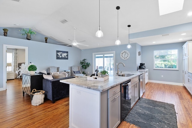 kitchen featuring light stone countertops, sink, light hardwood / wood-style floors, lofted ceiling with skylight, and a kitchen island with sink