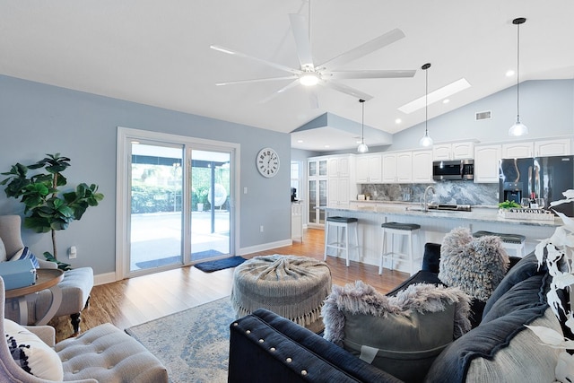 living room with lofted ceiling with skylight, ceiling fan, and light hardwood / wood-style flooring