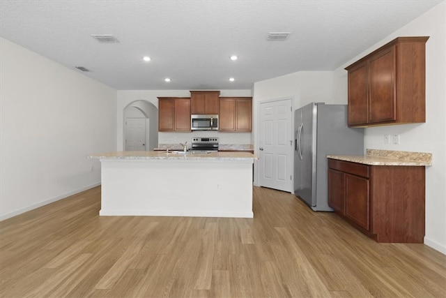 kitchen with a textured ceiling, light wood-type flooring, stainless steel appliances, and a center island with sink