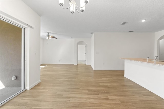 unfurnished living room with a textured ceiling, ceiling fan with notable chandelier, light hardwood / wood-style floors, and sink