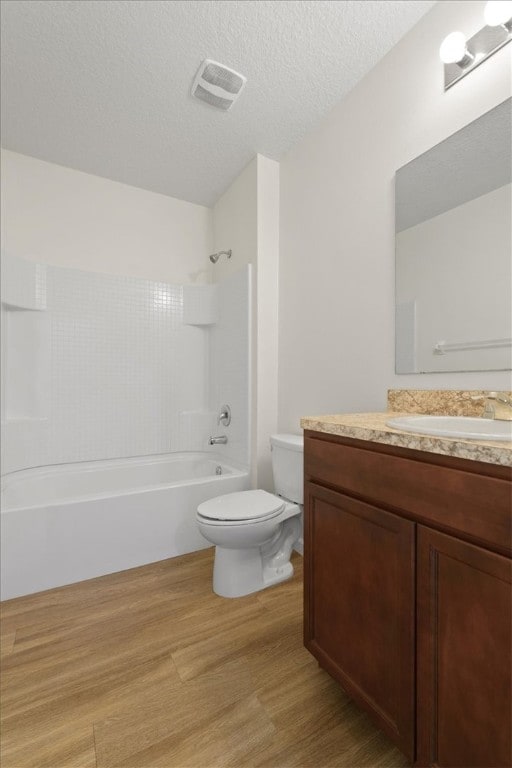 full bathroom with hardwood / wood-style floors, a textured ceiling, toilet, vanity, and shower / bathtub combination