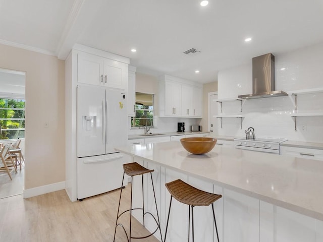 kitchen featuring white cabinetry, wall chimney exhaust hood, a healthy amount of sunlight, and white appliances