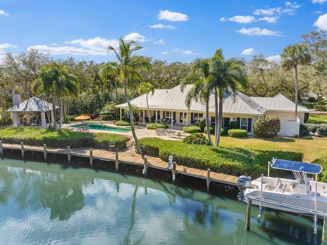 back of house featuring a water view, metal roof, an outdoor pool, and a patio