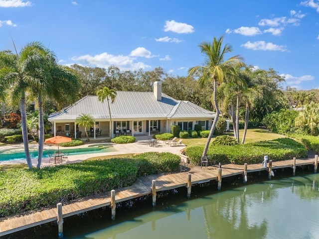 back of property with a patio area, a water view, an outdoor pool, and metal roof