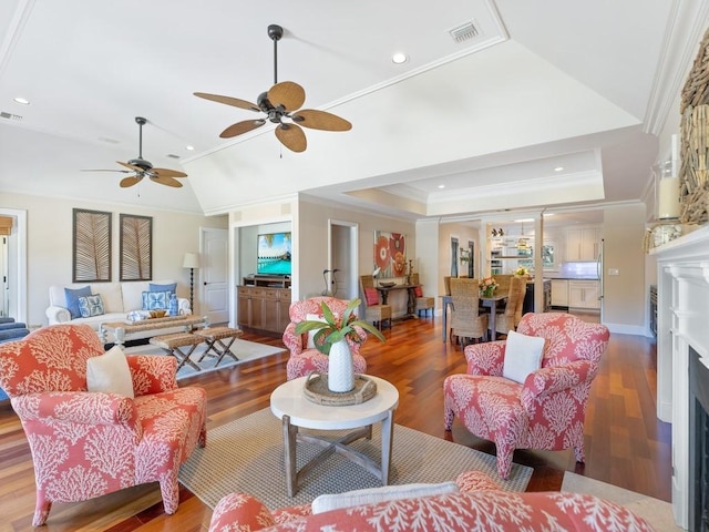 living room with visible vents, a raised ceiling, wood finished floors, crown molding, and a fireplace