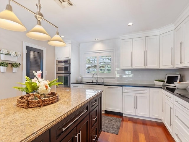 kitchen featuring decorative light fixtures, visible vents, double oven, white cabinetry, and a sink