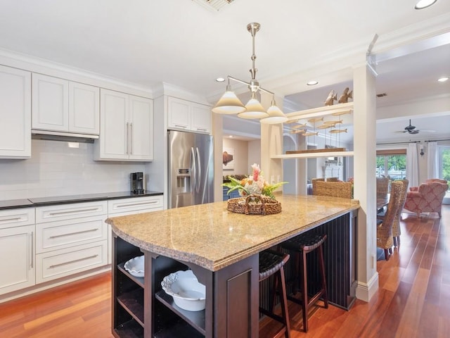 kitchen featuring stainless steel fridge, white cabinets, dark stone countertops, wood finished floors, and open shelves