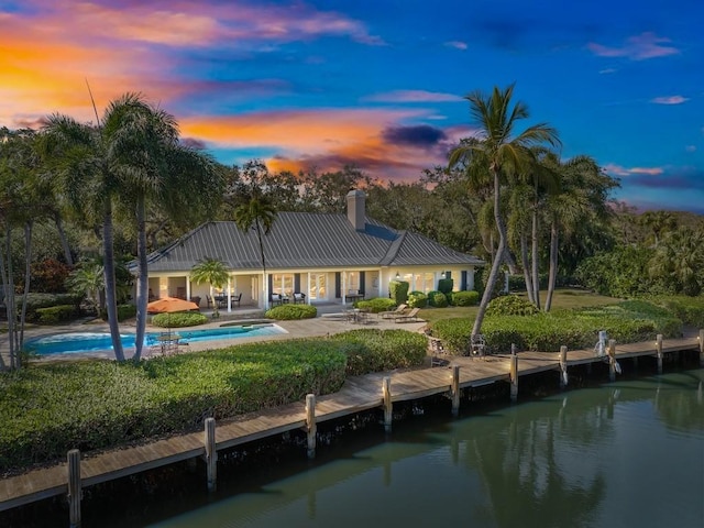 rear view of property with metal roof, a patio, a chimney, and an outdoor pool