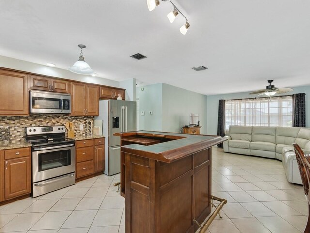 kitchen with appliances with stainless steel finishes, pendant lighting, light tile patterned floors, and backsplash