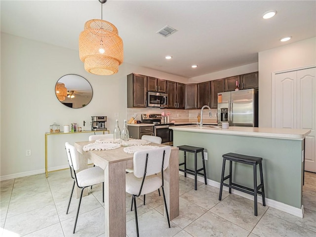 kitchen featuring stainless steel appliances, dark brown cabinets, a kitchen island with sink, and decorative light fixtures