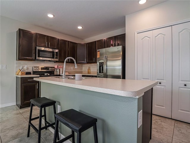 kitchen featuring backsplash, dark brown cabinets, stainless steel appliances, and a breakfast bar