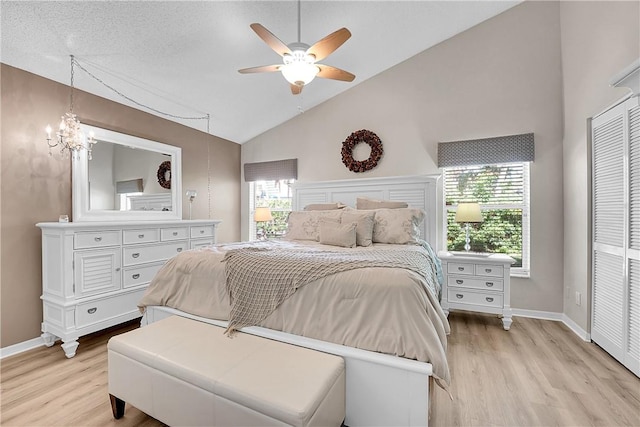 bedroom featuring ceiling fan with notable chandelier, light hardwood / wood-style floors, a textured ceiling, and high vaulted ceiling