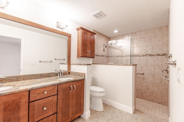 bathroom featuring vanity, tile patterned flooring, toilet, a textured ceiling, and a tile shower