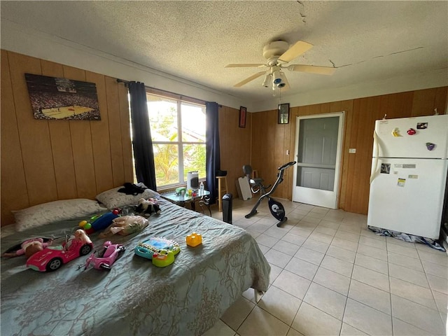 bedroom with wood walls, a textured ceiling, light tile patterned floors, white fridge, and ceiling fan