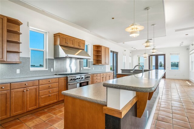 kitchen featuring backsplash, stainless steel stove, hanging light fixtures, and a kitchen island with sink