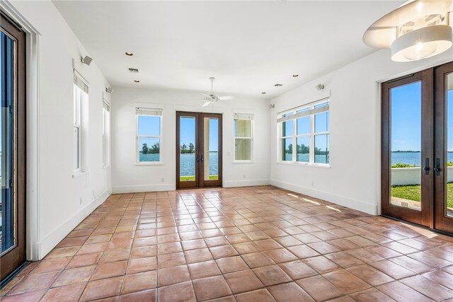 tiled spare room featuring a healthy amount of sunlight, a water view, and french doors