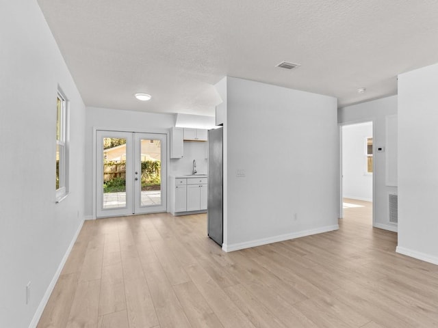 interior space with a textured ceiling, french doors, light hardwood / wood-style flooring, and sink