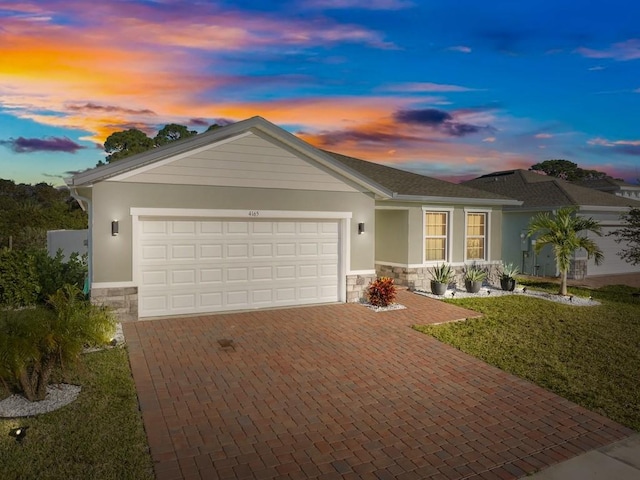 ranch-style house featuring decorative driveway, stucco siding, a lawn, a garage, and stone siding