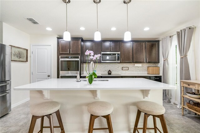 kitchen with hanging light fixtures, a kitchen island with sink, dark brown cabinets, and stainless steel appliances