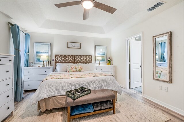 bedroom with light wood-type flooring, a tray ceiling, and ceiling fan