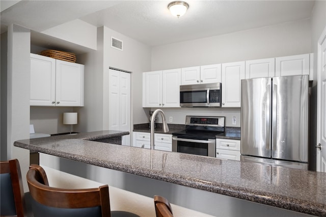 kitchen with dark stone counters, white cabinetry, a breakfast bar, and stainless steel appliances