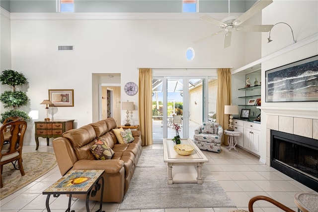 living room with a tile fireplace, ceiling fan, light tile patterned floors, and a high ceiling