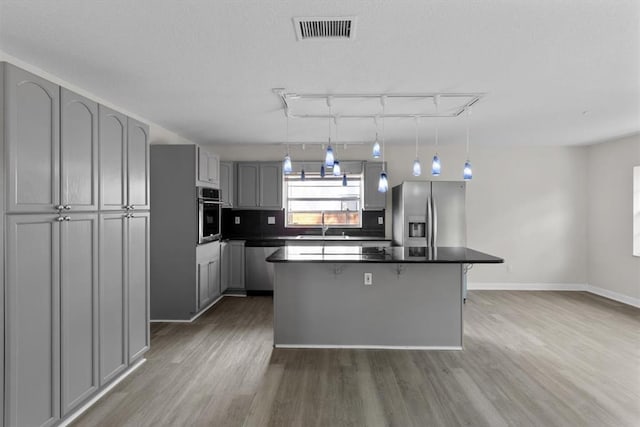 kitchen featuring hanging light fixtures, appliances with stainless steel finishes, gray cabinets, a kitchen island, and backsplash