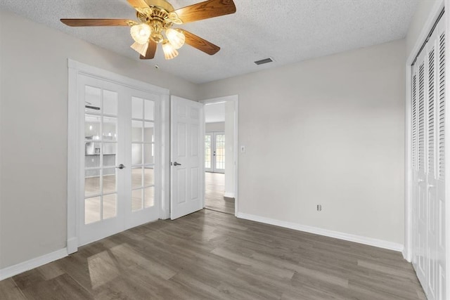 unfurnished bedroom with ceiling fan, dark hardwood / wood-style floors, a textured ceiling, french doors, and a closet