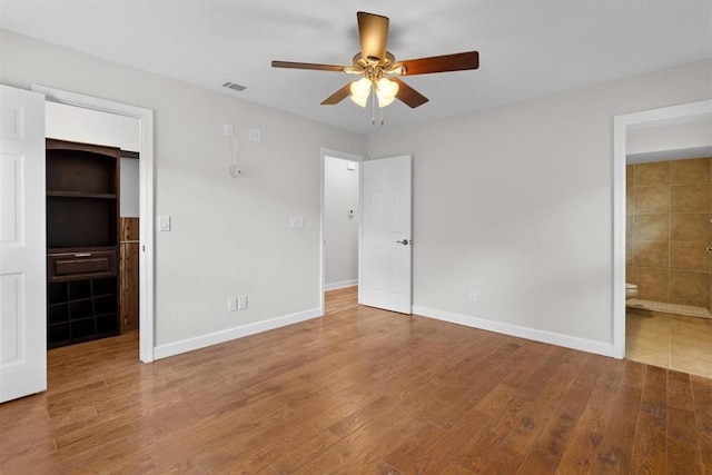 unfurnished bedroom with a walk in closet, wood-type flooring, ensuite bathroom, and a closet