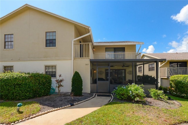 view of front of house with a balcony, ceiling fan, stucco siding, and a front yard