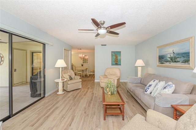 living area featuring wood finished floors, a ceiling fan, a chandelier, a textured ceiling, and baseboards