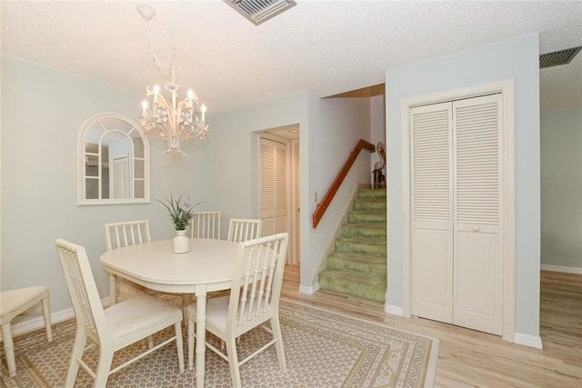 dining space with light wood finished floors, a chandelier, stairs, baseboards, and a textured ceiling