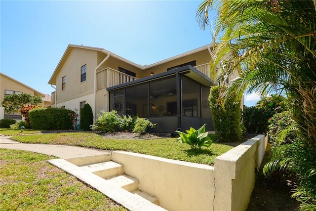 back of house with a sunroom, stucco siding, a balcony, ceiling fan, and a lawn