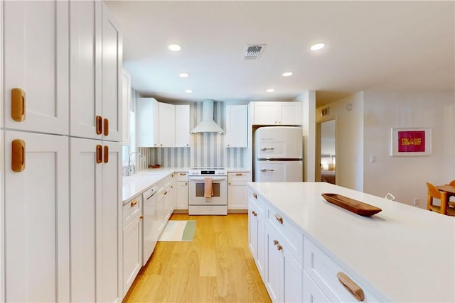 kitchen featuring white appliances, light hardwood / wood-style flooring, backsplash, wall chimney range hood, and white cabinets