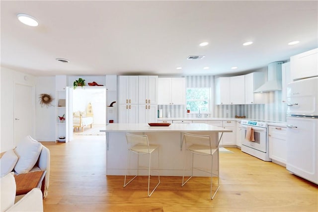 kitchen with a center island, white appliances, white cabinets, a breakfast bar area, and wall chimney range hood