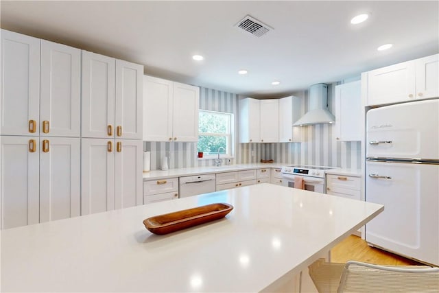 kitchen with white appliances, sink, wall chimney exhaust hood, and white cabinetry