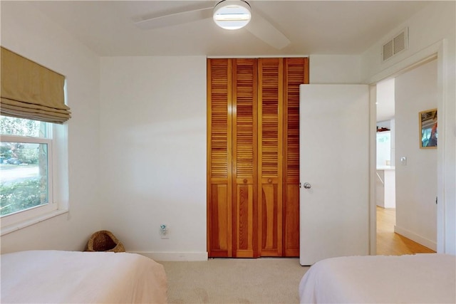 bedroom with ceiling fan, light carpet, and a closet