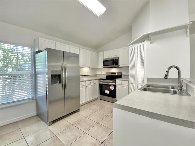 kitchen with sink, light tile patterned flooring, lofted ceiling, white cabinets, and appliances with stainless steel finishes